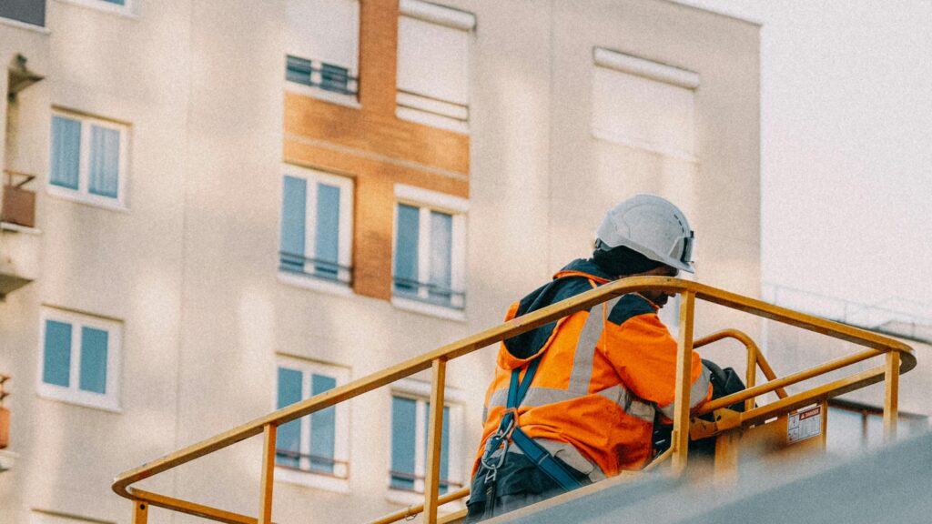 News A construction worker in safety gear operates a lift near an apartment building.