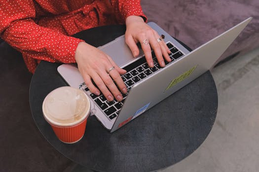 A woman in a red polka dot dress typing on a laptop with coffee nearby.