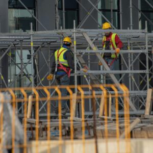 Two construction workers wearing safety gear and helmets working on scaffolding outdoors.