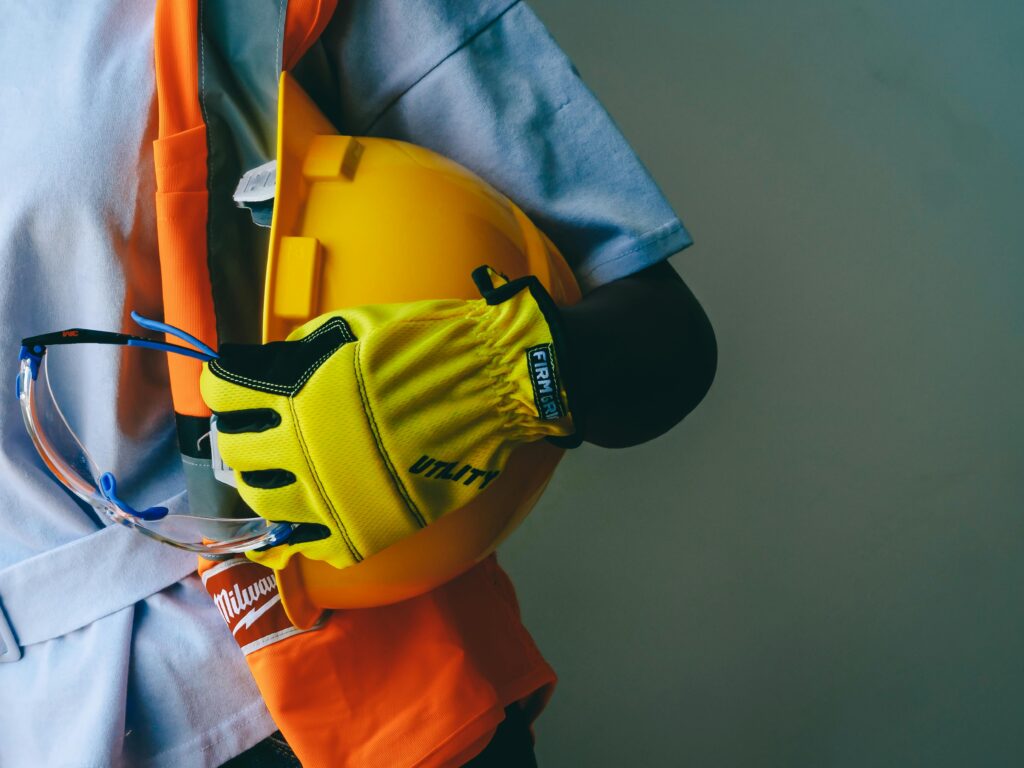 News Close-up of a construction worker holding a hardhat and wearing PPE, including gloves and goggles.