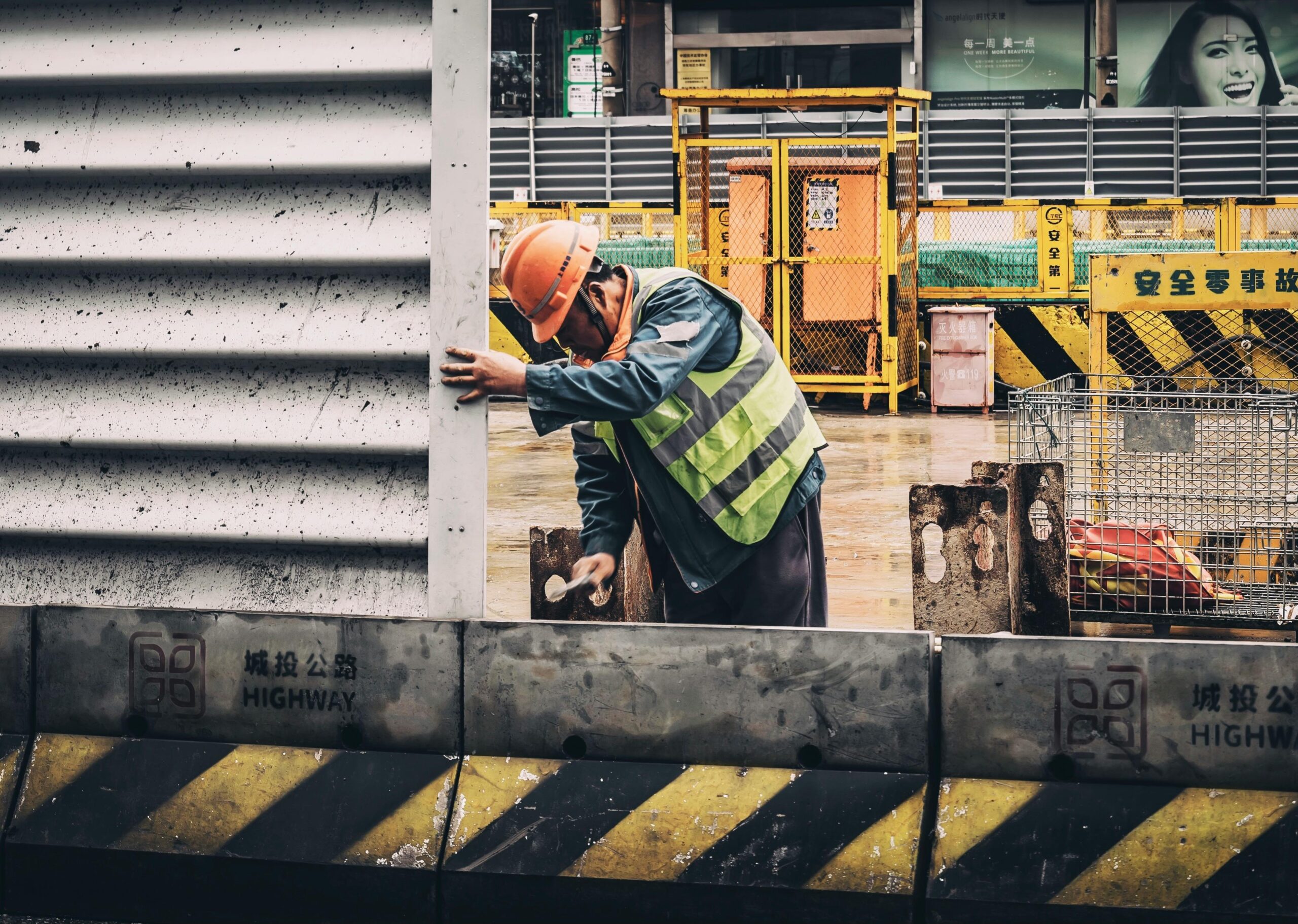 A construction worker in a reflective vest and hard hat at a busy urban construction site.